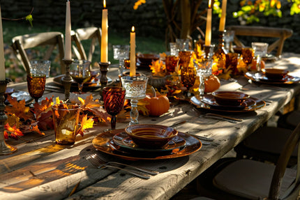 Rustic outdoor Thanksgiving table decor with amber glassware, candles, and fall leaves for a cozy setting.