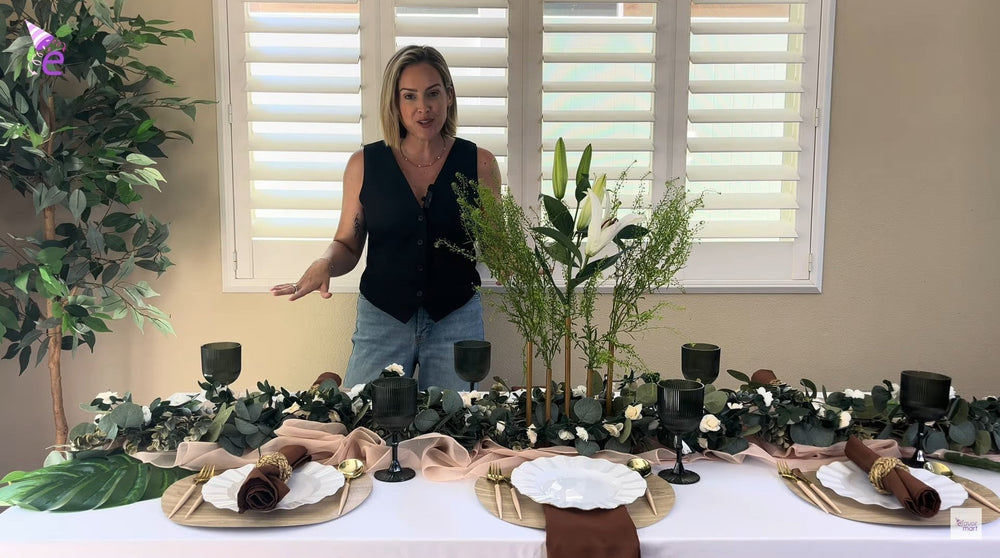 Completed boho table setting with green glasses, flowers, and gold utensils.