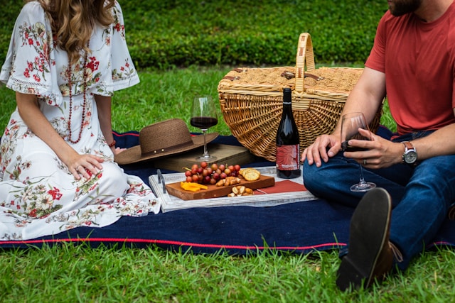 A couple enjoys a fall picnic with wine, grapes, and cheese on a blanket.