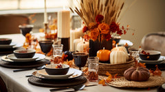 Fall table decor with black dinnerware, candles, pumpkins, and a wheat and rose centerpiece.