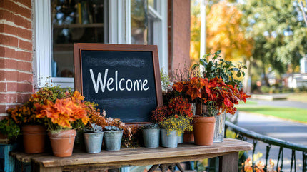 A welcoming fall decor display featuring vibrant orange leaves, potted plants, and a chalkboard sign.