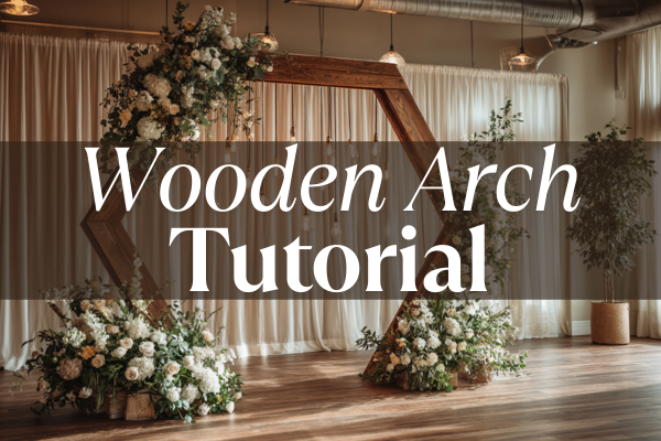 Indoor floral wedding display with a hexagonal wooden arch and draped curtains.